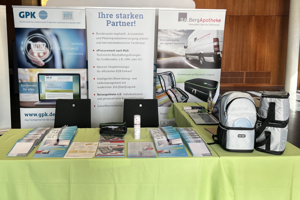 Messe-Stand-2024 Messestand der GPK und BA.BergApotheke mit Banner 'Ihre starken Partner!' und Informationen zu eProcurement, Reiseapotheke 2.0 und Logistiklösungen, Laptop auf schwarzem Tisch, verschiedene medizinische Produkte auf grünem Tisch.